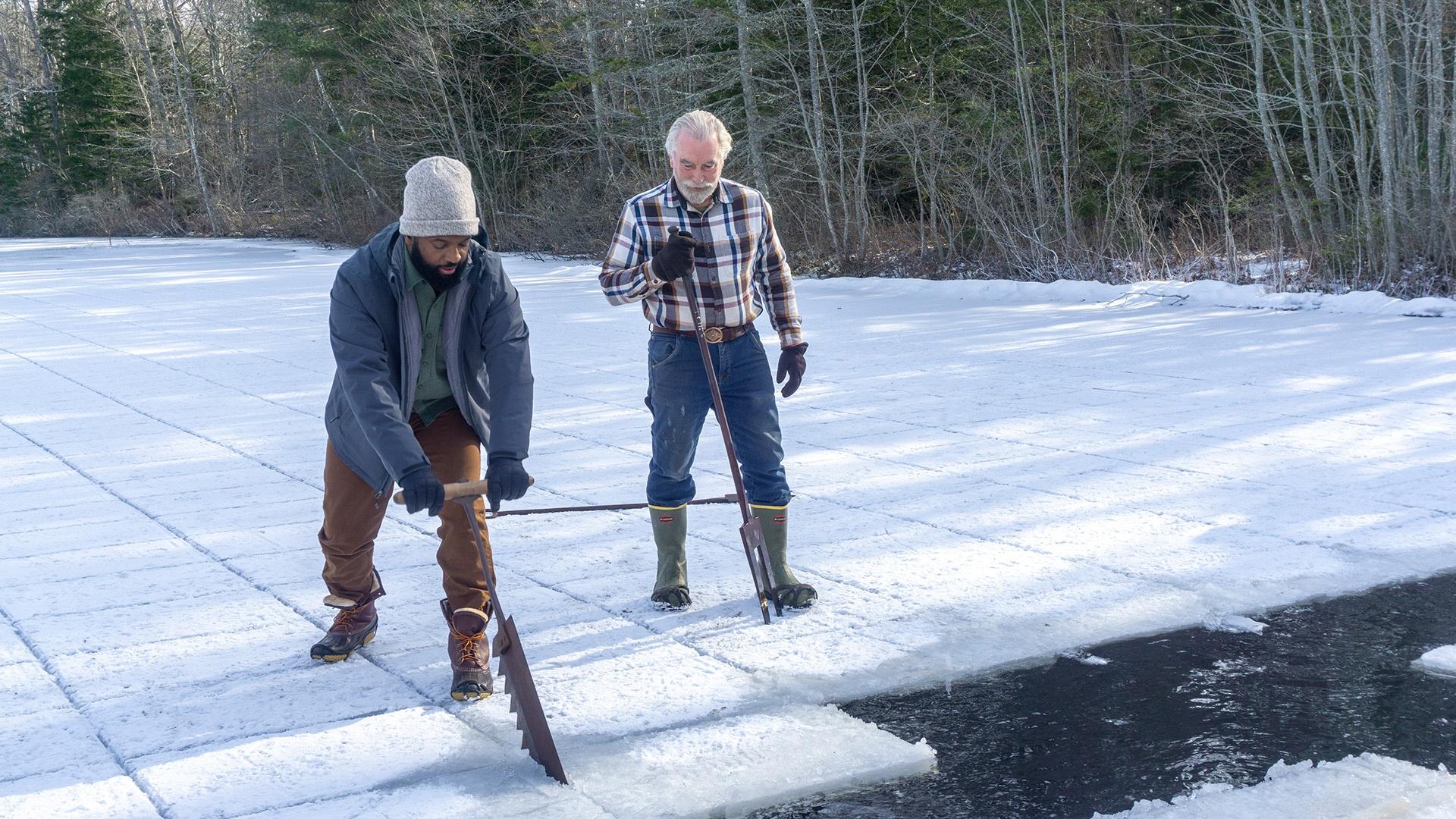 Baratunde sawing ice while Ken stands next to him