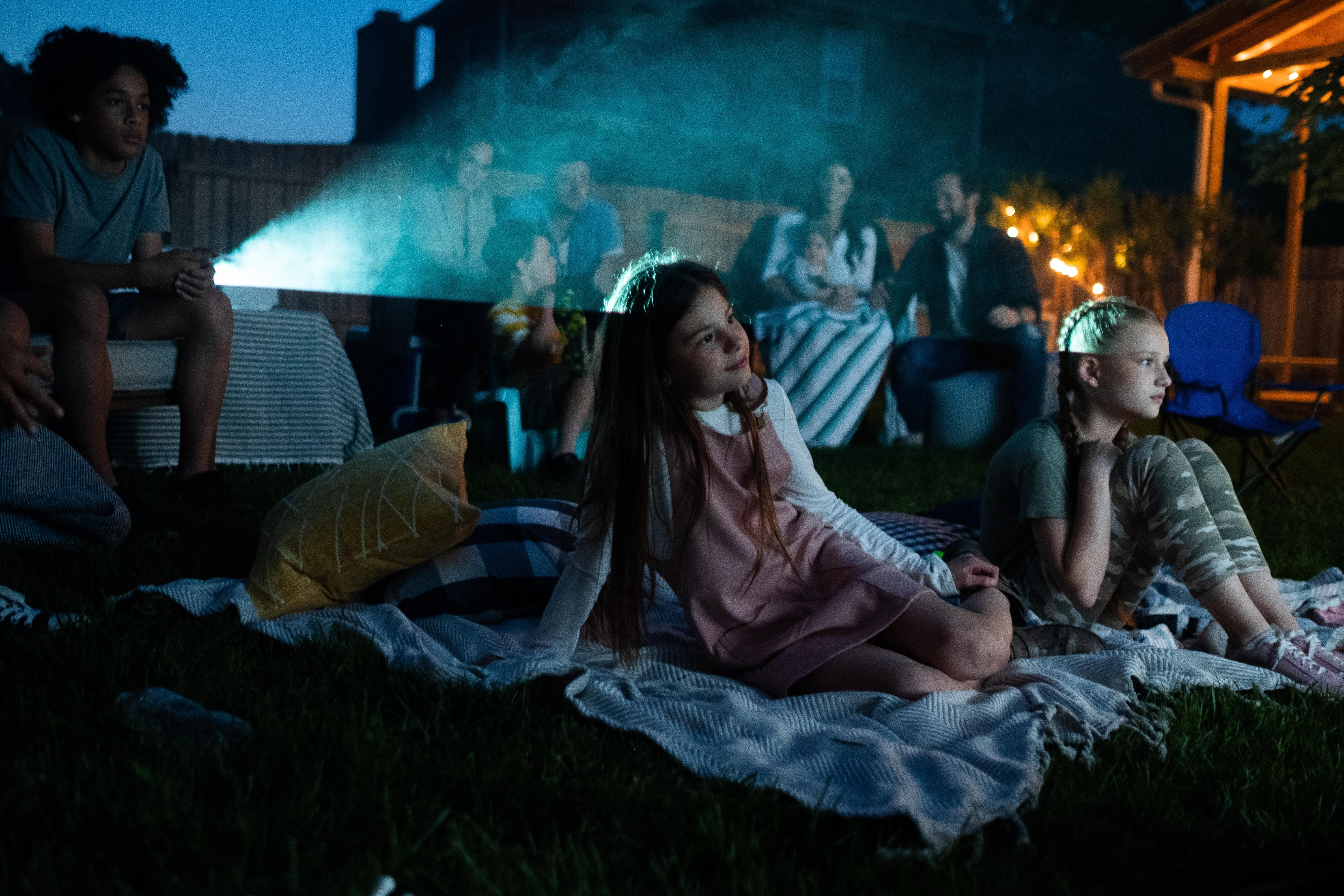 Crowd of adults and kids sit outside and watch a film on a projector